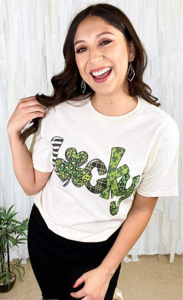 Model wearing our lucky print tee. The tee is short sleeve and white with the word lucky. The word is bold and filled in with different green prints inside. The "u" is a clover.