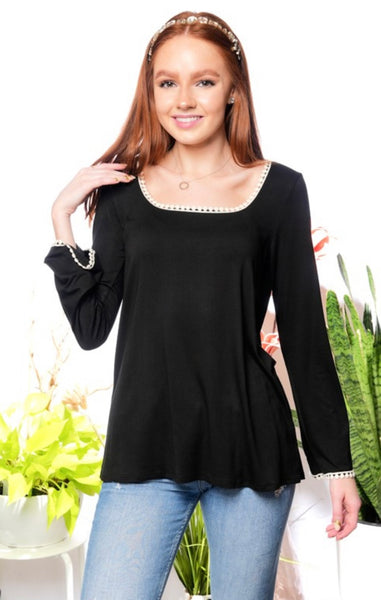 Model wearing a black crochet accent top. Top is long sleeve and black with white crochet accent on the neckline and wrist. Model pairs the top with light wash jeans, a necklace, and headband.